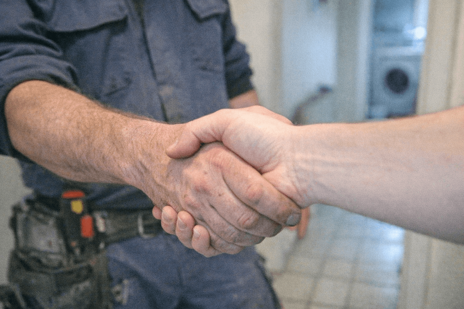 Kundin und Handwerker stehen im Hausflur und reichen sich nach einer abgeschlossenen Serviceleistung die Hand